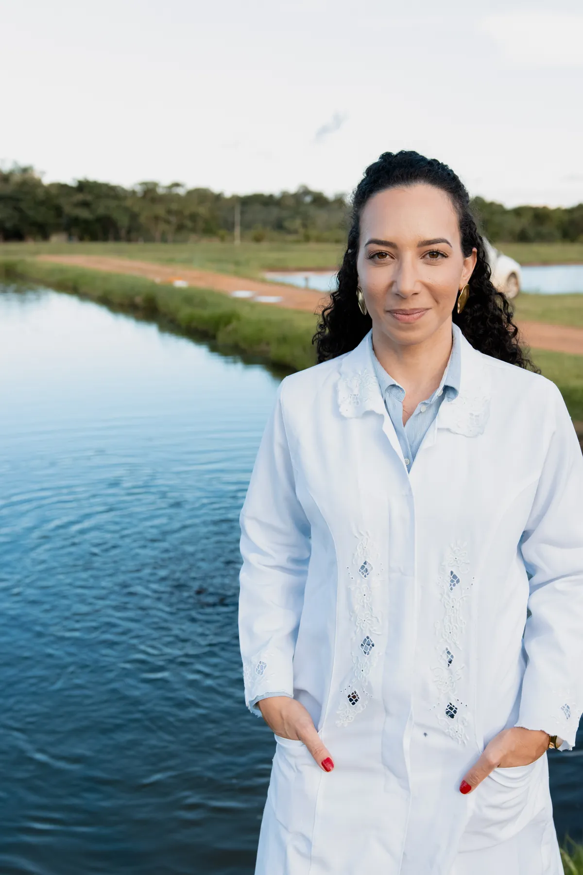 Soraia Dall'Agnol, de jaleco branco, às margens de um viveiro de piscicultura