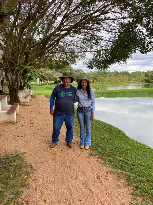 Soraia ao lado de um produtor rural, com um lago ao fundo