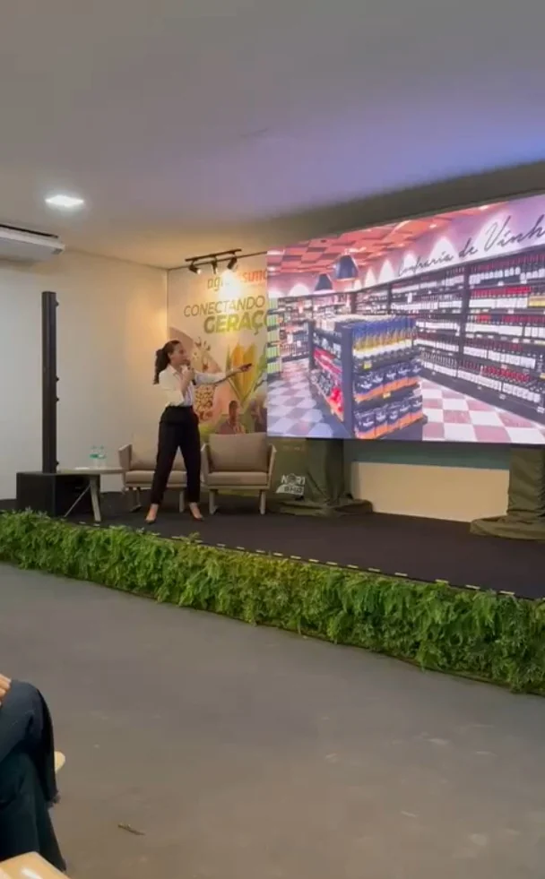 Soraia no palco, apontando para o telão durante uma palestra